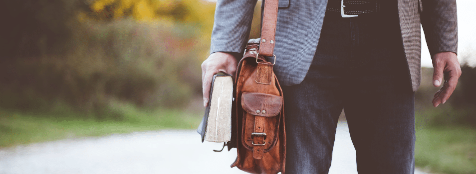 A man walking outside with a Bible and bag in hand