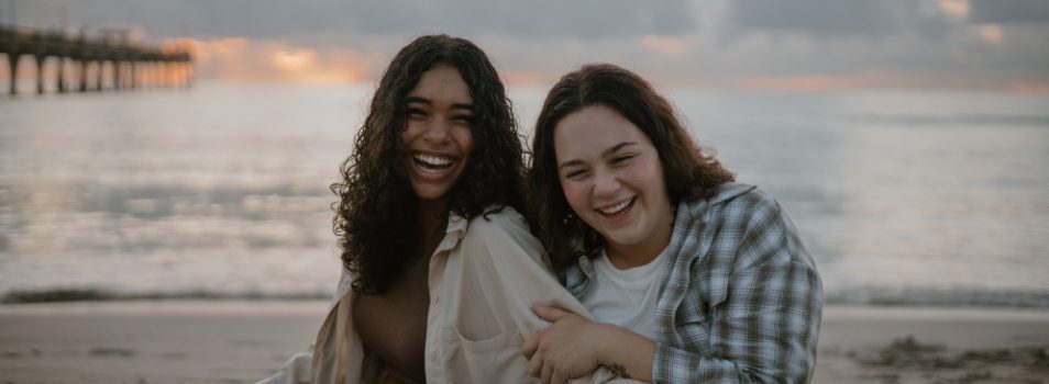 Two women sitting on sand grinning