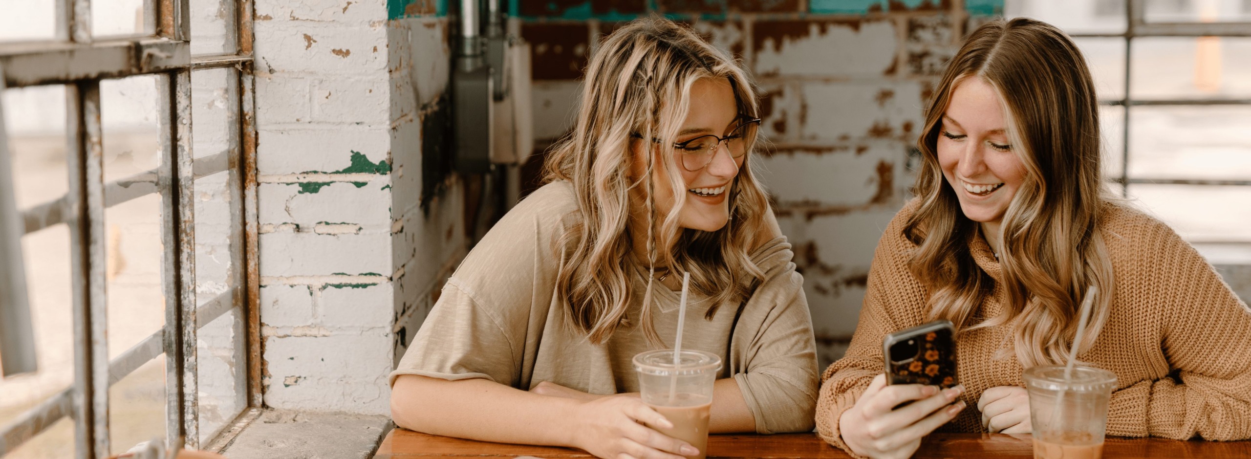 two women smiling down at smartphone in a coffeeshop