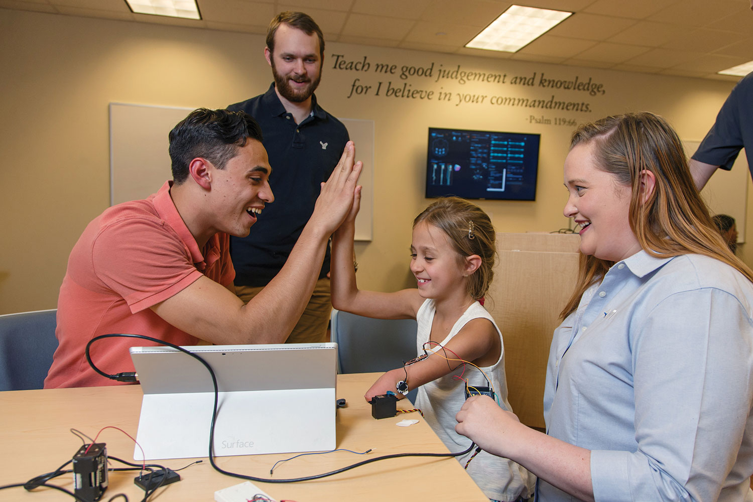 Maddie Rebsamen, an 8-year-old bionic hand recipient, gets a high five from rising computer engineering junior Adam Morrone. Recent biomedical sciences graduate Mitchell Reynolds and Davis help test electric signals from Maddie’s muscles.