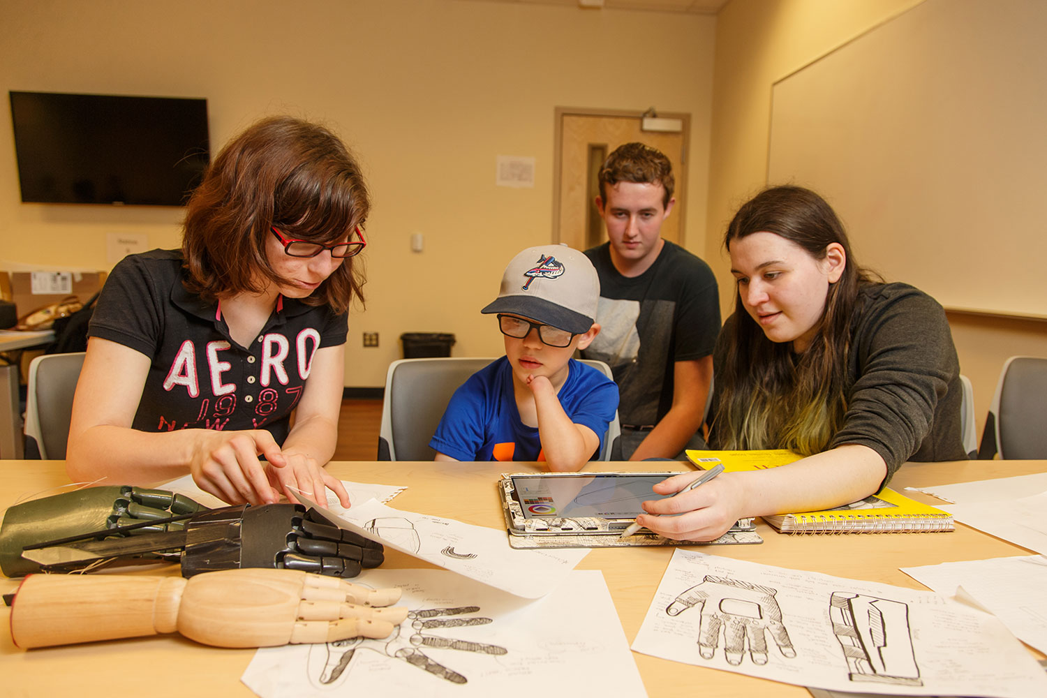 The aesthetics team — Jefferson Forest High School rising juniors Natalia Griffis (left), Jessy Watson, and Juliet Hatch — show Connor McCombs some design ideas for his EXO-Arm.