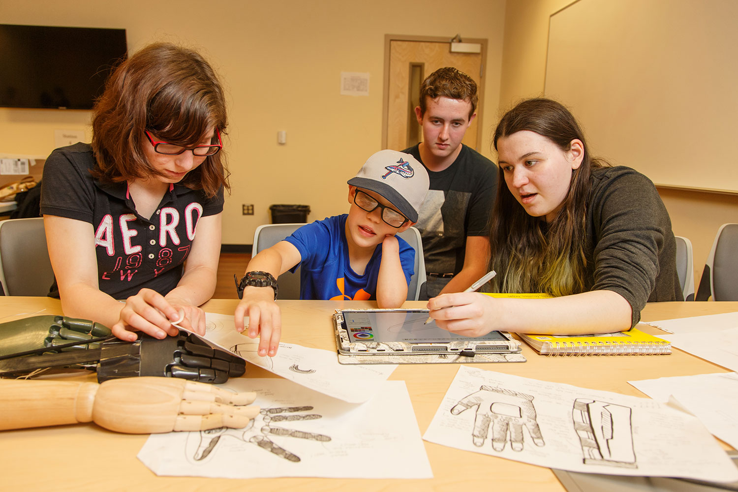 The aesthetics team — Jefferson Forest High School rising juniors Natalia Griffis (left), Jessy Watson, and Juliet Hatch — show Connor McCombs some design ideas for his EXO-Arm.