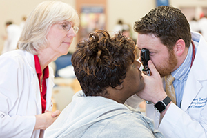 LUCOM student-doctor examines eye of patient.