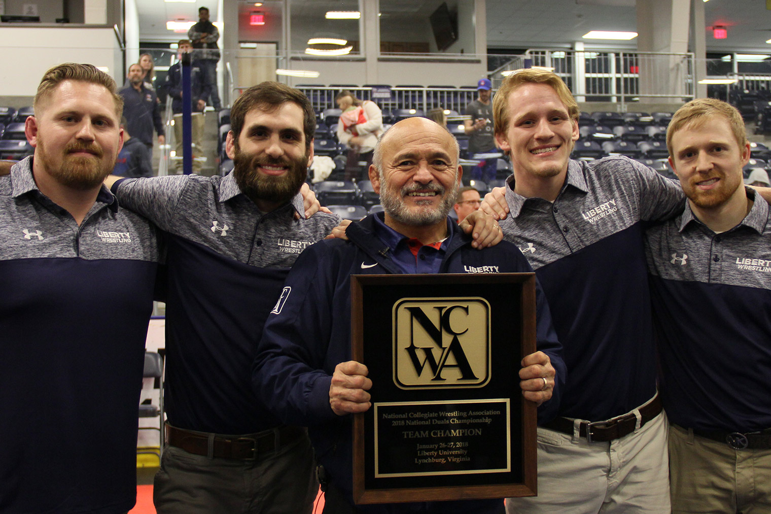 Liberty Head Coach Jesse Castro holds the NCWA National Duals plaque flanked by his assistant coaches. (Photo by Patrick Strawn)
