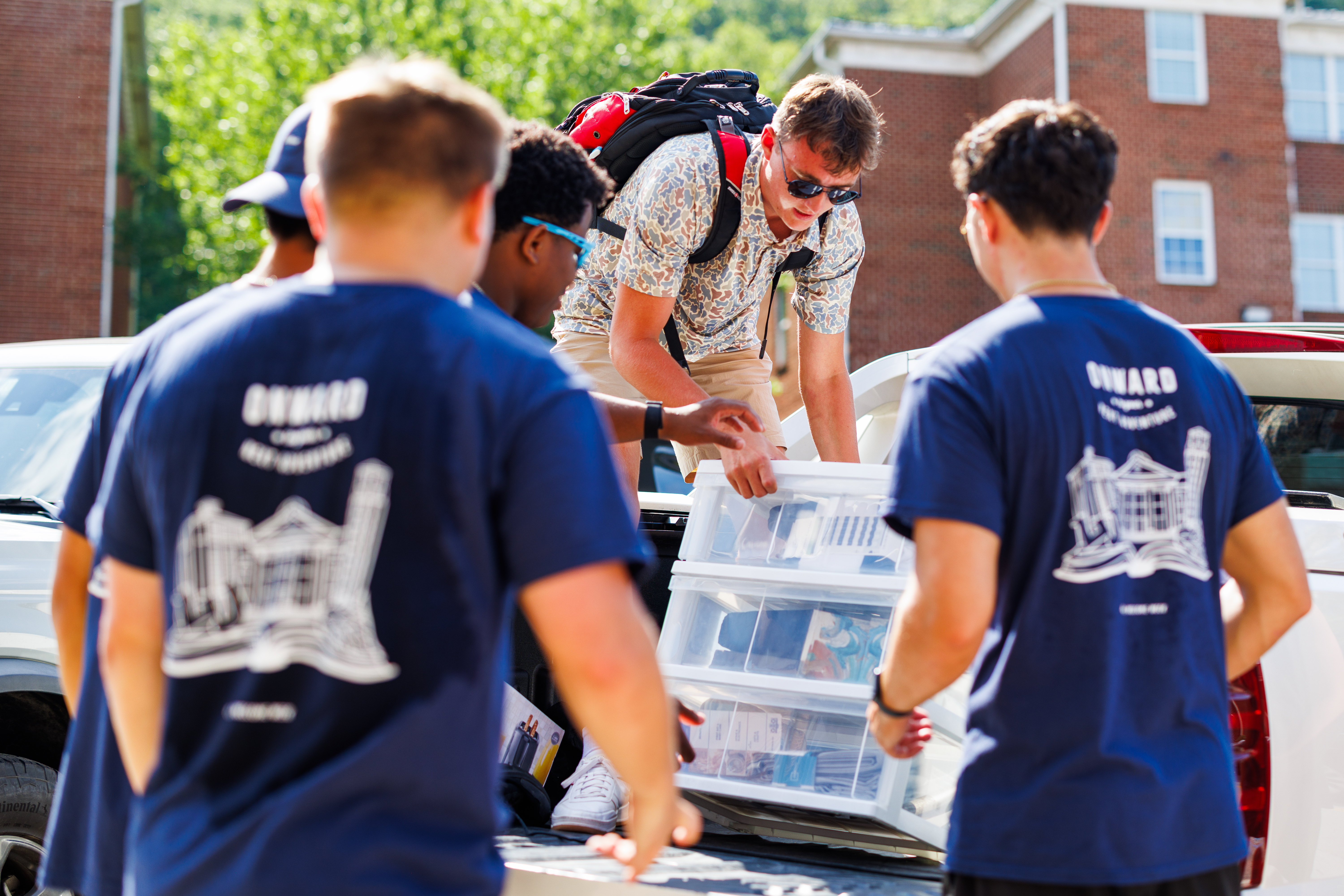 Several individuals in matching blue shirts are loading supplies into the back of a white vehicle outdoors.