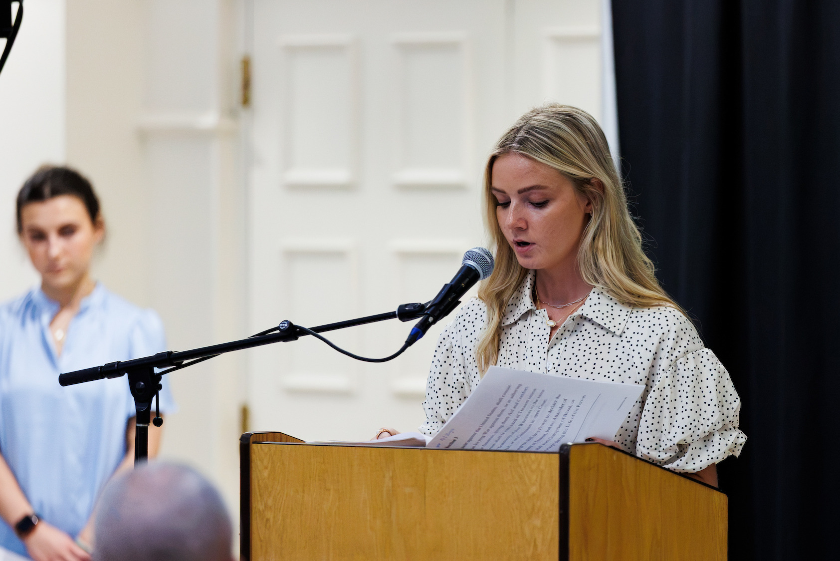 A person speaks at a podium bearing the name "Liberty University," while another individual stands nearby.