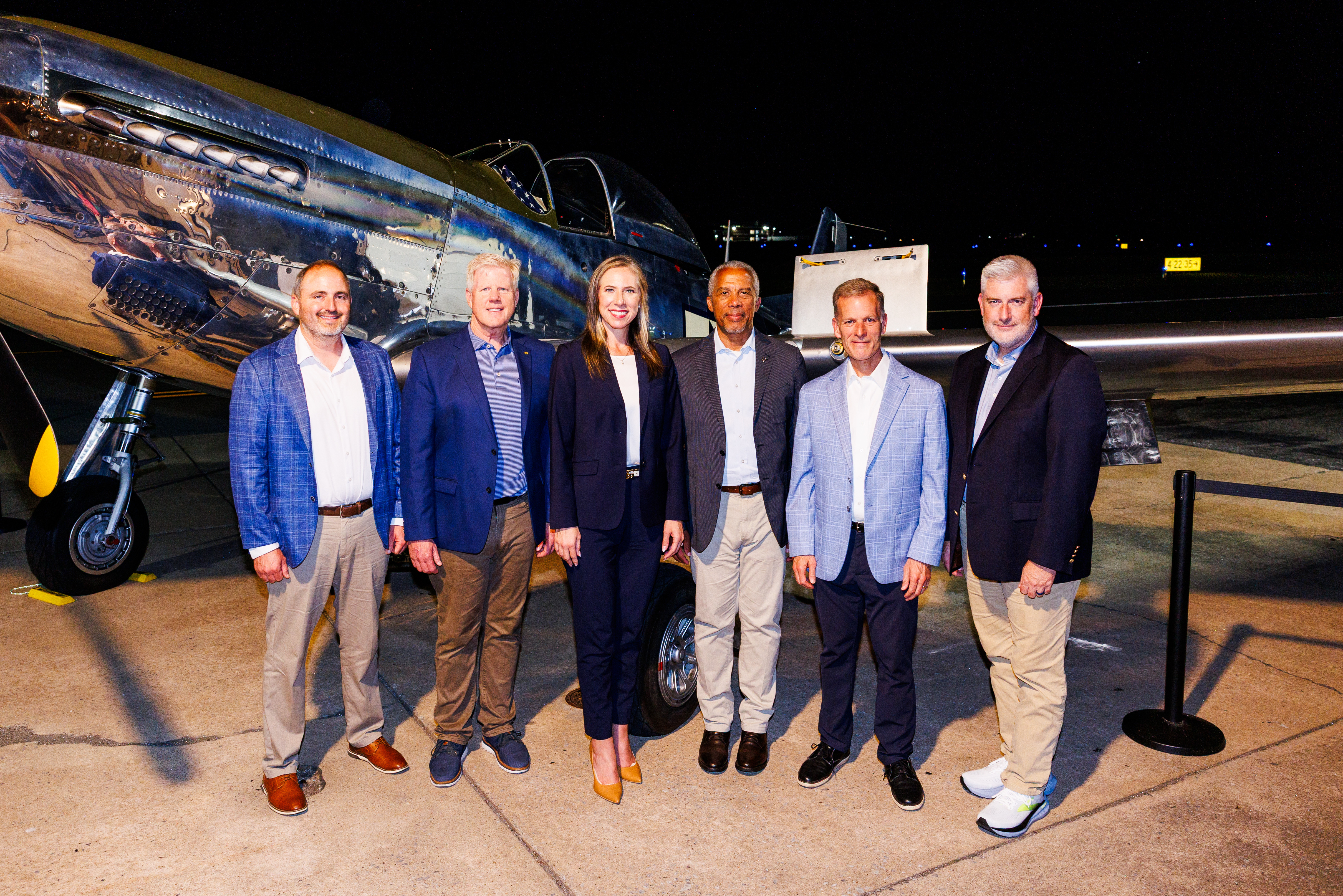 Six individuals pose for a photo in front of a vintage aircraft at night.