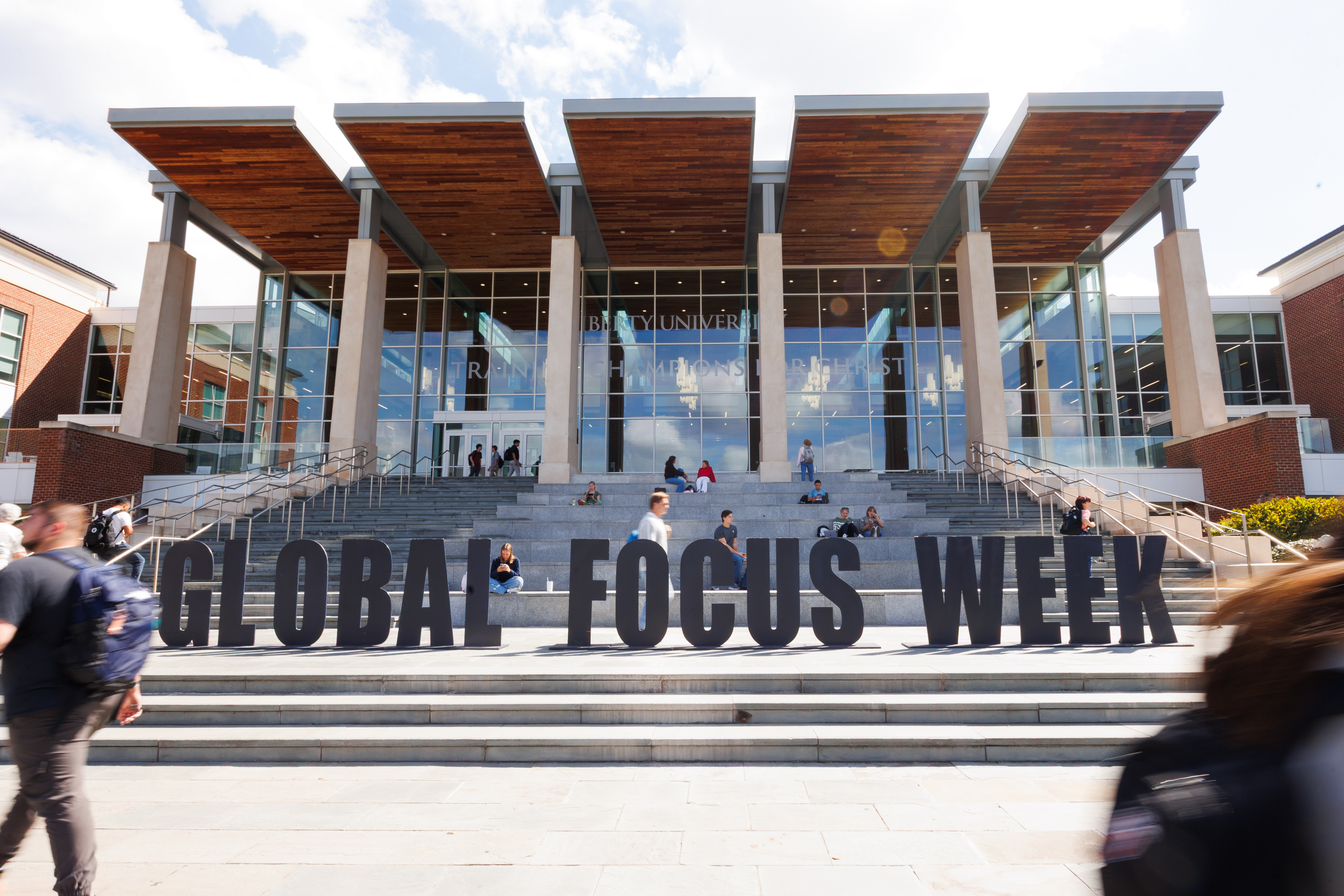 Students gather on steps in front of a modern university building with large "GLOBAL FOCUS WEEK" letters.