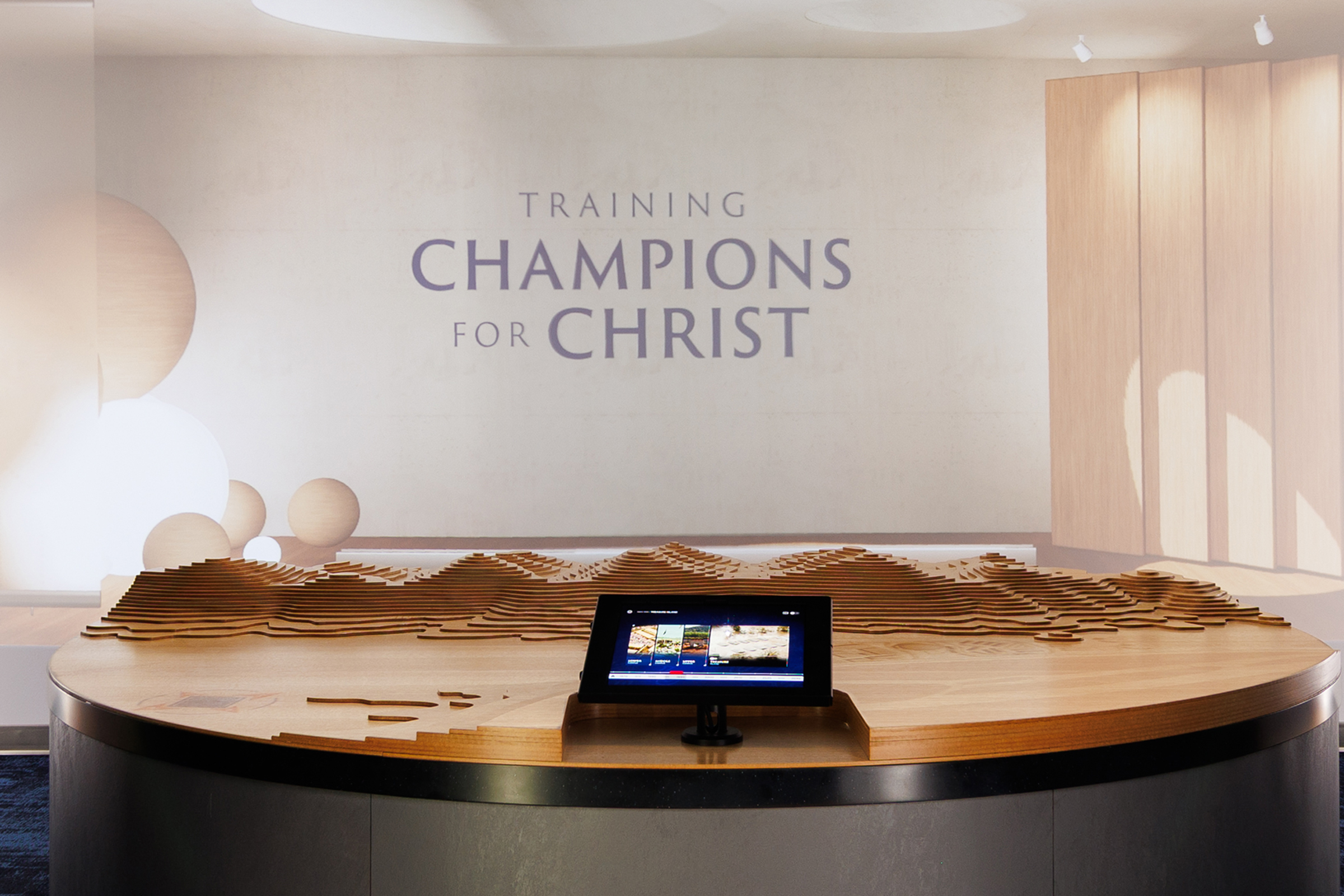 A modern circular reception desk sits in a spacious lobby with red-accented walls and a large projection screen displaying "Liberty University" and "Training Champions for Christ."