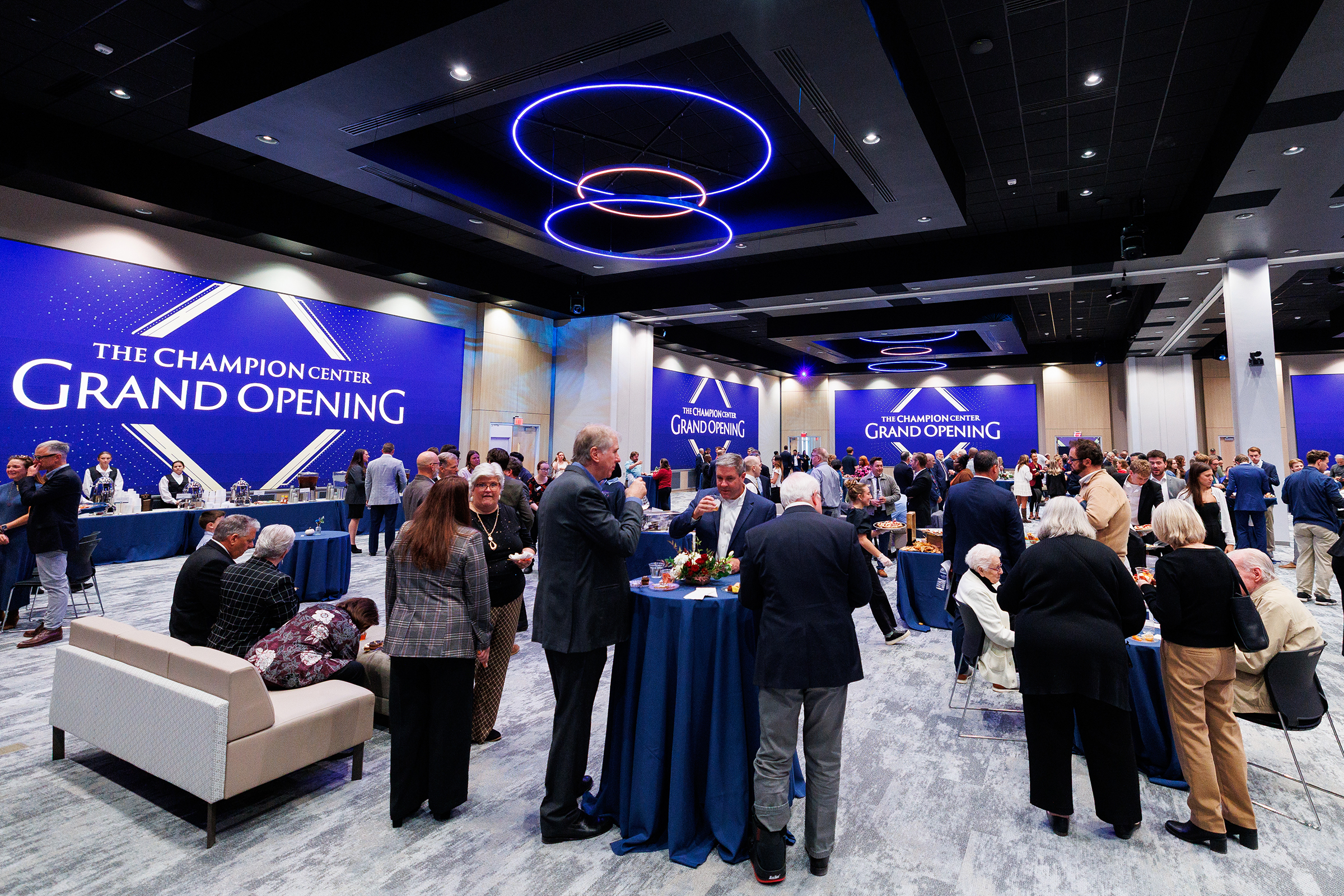 Attendees mingle and socialize at the grand opening of The Champion Center, with blue-themed decor and modern lighting.