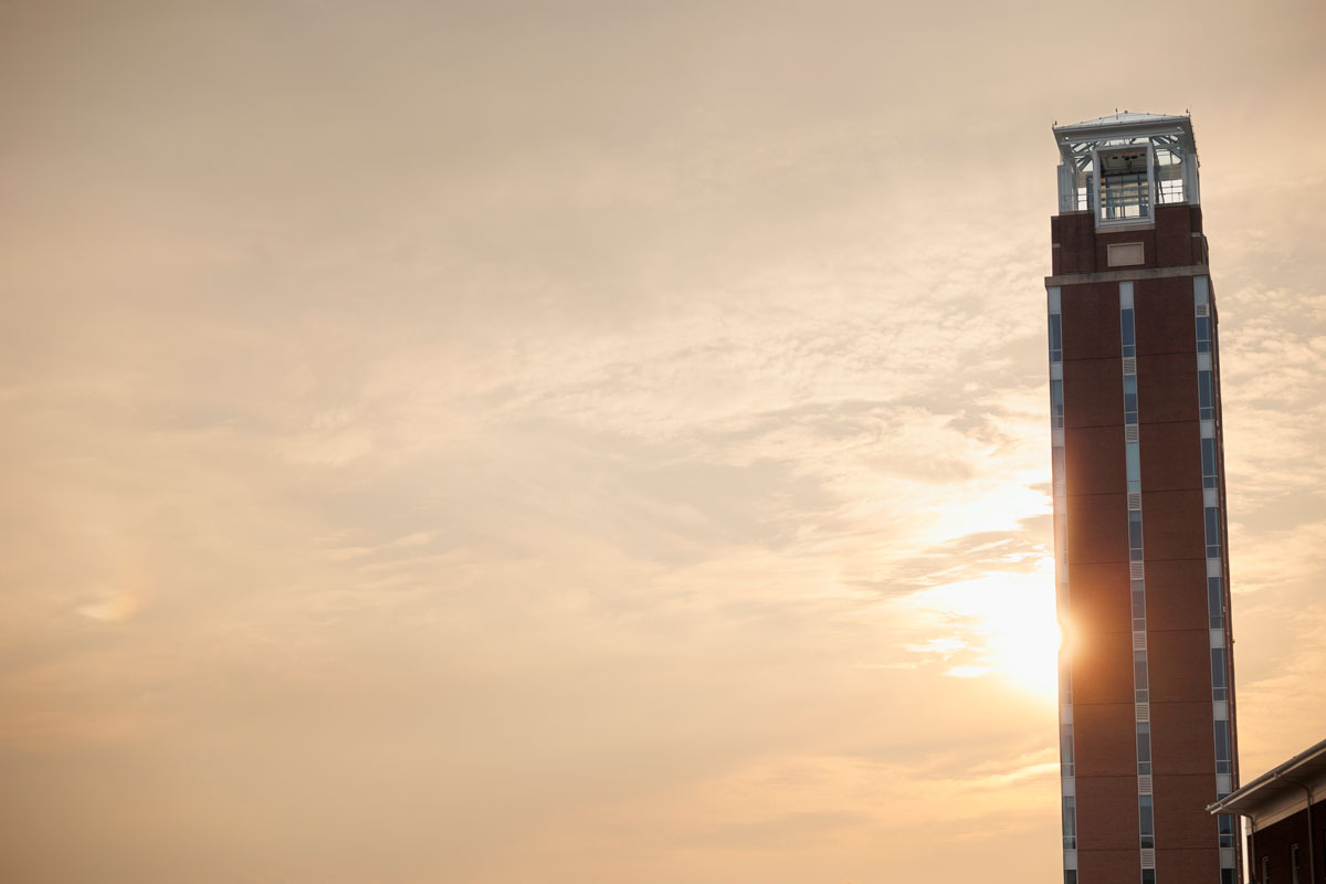 A tall brick tower stands against a warm, golden sunset sky with soft clouds.