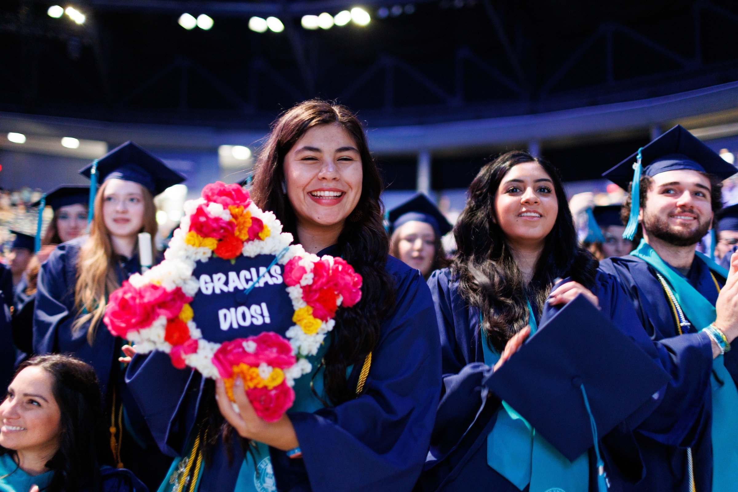Female LUOA graduate showing her cap decorated with flowers and the words "Gracias Dios!"