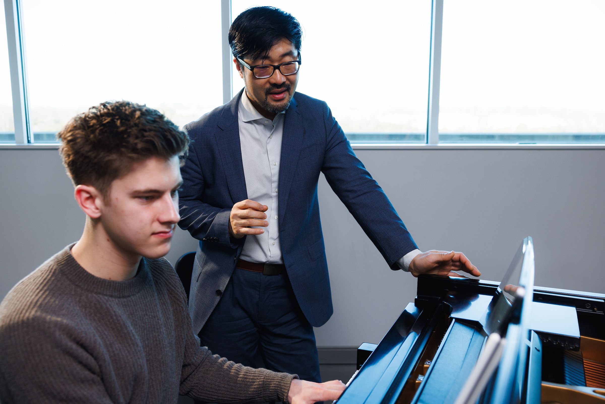 A music professor giving a student instruction at a piano