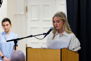 A person speaks at a podium bearing the name 