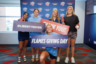 Five individuals pose in front of a branded backdrop holding signs that read 